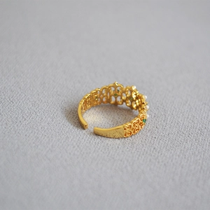 Detail view of a vintage gold lace ring with emerald gemstones and pearls on gray fabric