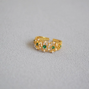 Macro detail of vintage gold lace ring with emerald stones and pearls in Victorian style