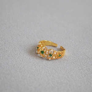Detail of vintage gold lace ring with emerald gemstone and delicate pearls