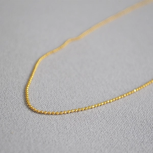 Close-up of minimalist gold beaded necklace showing textured metallic beads and finish