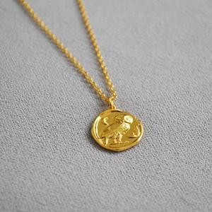 Golden owl and crescent moon relief pendant necklace on textured fabric background