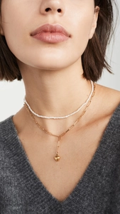 Detail of layered gold paperclip chain and pearl necklace with heart pendant on model