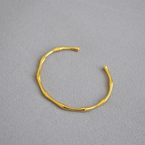 Detailed close-up of a gold-plated bamboo joint bangle on a textured background