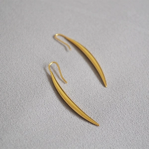 Detail of minimalist gold plated crescent drop earrings with a matte metallic finish