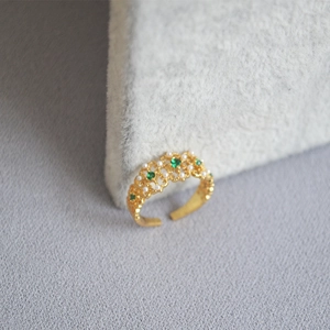 Detailed close-up of emerald and pearl vintage gold ring with floral lace patterns