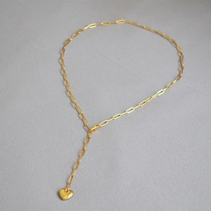 Close-up of golden paperclip chain Y-necklace with polished heart pendant detail