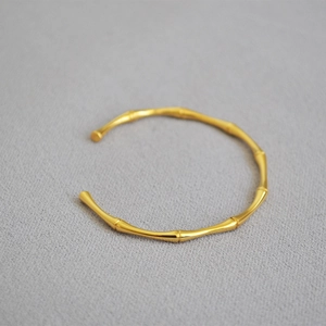 Macro shot of gold-plated bamboo joint bangle on textured grey fabric background