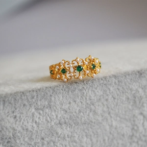 Macro detail of vintage gold ring with emerald stones, pearls and ornate lace carving