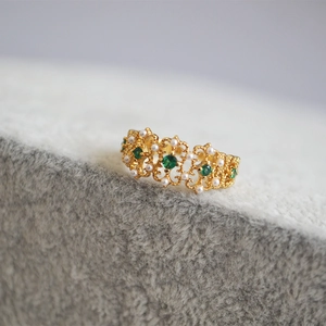 Macro detail of vintage gold ring with emerald stones and pearls in lace setting
