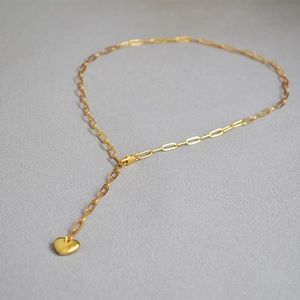 Detail of golden paperclip chain necklace with a solid heart pendant on a gray surface