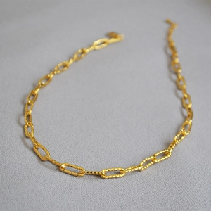 Collier chaîne trombone dorée avec finition martelée texturée sur fond neutre