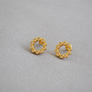 Minimalist gold hoop earrings with zircon stones on a gray textured background