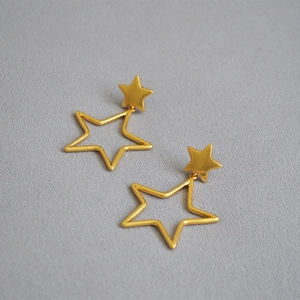 Detailed view of gold hollow star earrings with double celestial layering on grey fabric