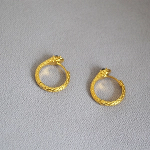 Macro shot of golden snake hoop earrings featuring detailed scales and dark stone eyes