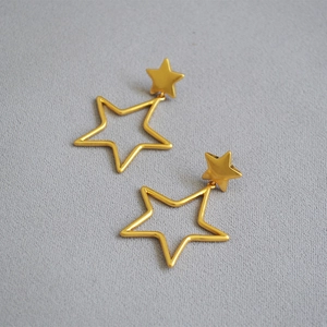 Detail of matte gold hollow star drop earrings featuring a geometric double star design