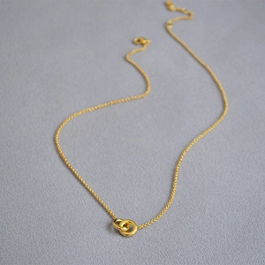 Macro detail of minimalist gold-plated interlocking double ring pendant on thin chain