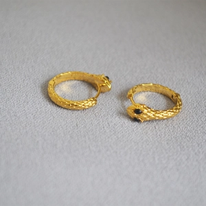 Close-up of golden snake hoop earrings with scale texture and black gemstone eyes