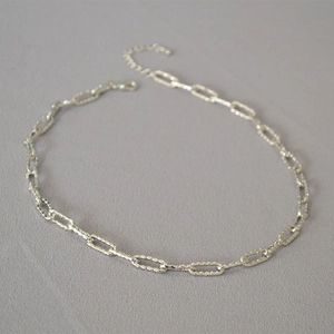 Détail d'un collier chaîne trombone argenté avec texture martelée et fermoir mousqueton