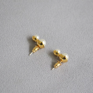 Minimalist gold peanut-shaped earrings with dual white pearls on grey textured fabric