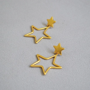 Close-up of golden hollow star drop earrings featuring a matte metallic finish on grey fabric