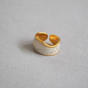 Detailed close-up of cream enamel ring with gold trim on gray textured background