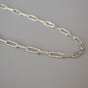Gros plan des maillons ovales texturés d'un collier en argent au fini métallique moderne