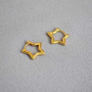 Detailed view of hollow gold-plated star-shaped hoop earrings on grey textured fabric