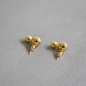 Macro detail of peanut-shaped double pearl gold-plated stud earrings on gray fabric