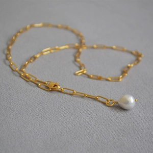 Detail of golden paperclip chain necklace featuring a white baroque pearl drop pendant