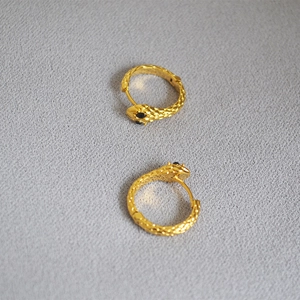 Detailed macro view of gold snake-shaped hoop earrings with scale texture and black stone eyes