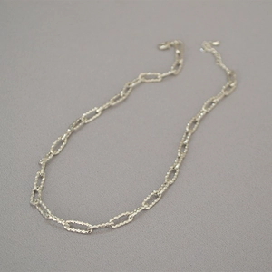 Détail d'un collier chaîne argentée à texture martelée avec fermoir mousqueton