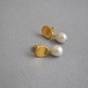 Detailed macro view of matte gold brass discs and white baroque pearls on silver studs