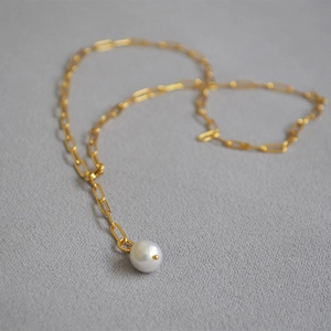 Macro view of a single white pearl pendant on a gold long-link chain necklace