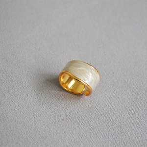 Detail of wide gold ring with white marble enamel texture on gray fabric background