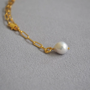Macro view of a gold paperclip chain and a natural white baroque pearl pendant