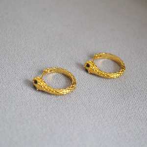 Detailed view of golden snake hoop earrings with scale texture and black crystal eyes