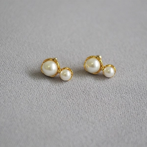 Detailed close-up of gold peanut-shaped double pearl earrings on gray fabric