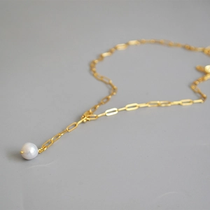 Macro view of a single white freshwater pearl on a golden paperclip chain necklace