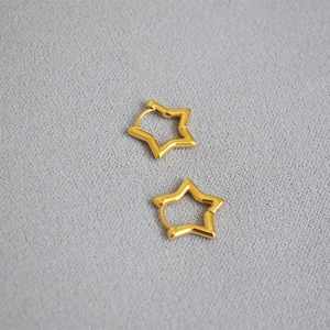 Detail of hollow star gold earrings on light grey fabric background showing elegant texture