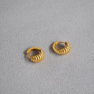 Macro shot of gold-plated croissant hoop earrings with ribbed texture on fabric