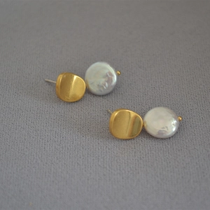 Detail of baroque pearl stud earrings with matte gold irregular metal discs on fabric