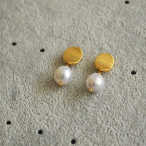 Detailed macro of baroque pearl earrings with matte gold plating on soft textured fabric