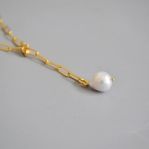 Detail of a gold paperclip chain necklace featuring a white baroque pearl pendant
