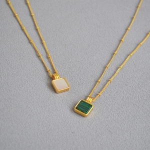 Détail de pendentifs carrés en malachite et nacre sur des chaînes à perles dorées