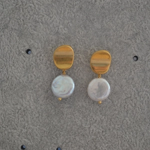 Detail of baroque pearl earrings with golden irregular brushed metal top and silver pins