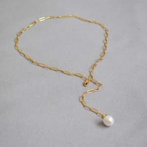Golden paperclip chain necklace with round white pearl pendant on a grey textured background