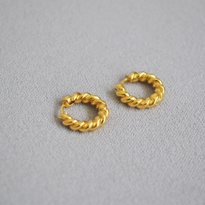 Boucles d'oreilles créoles torsadées plaquées or pour femme sur fond en tissu gris