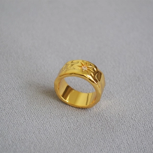 Macro detail of gold hammered band ring featuring an engraved north star with zircon