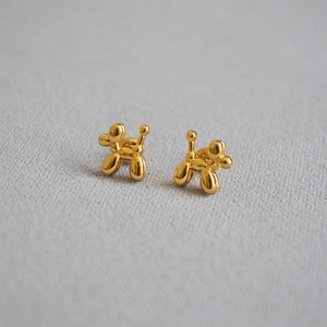 Minimalist golden 925 silver balloon poodle stud earrings on grey fabric background