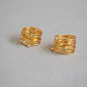 Detail of handmade layered gold rings with pearls and sparkling rhinestones on grey fabric